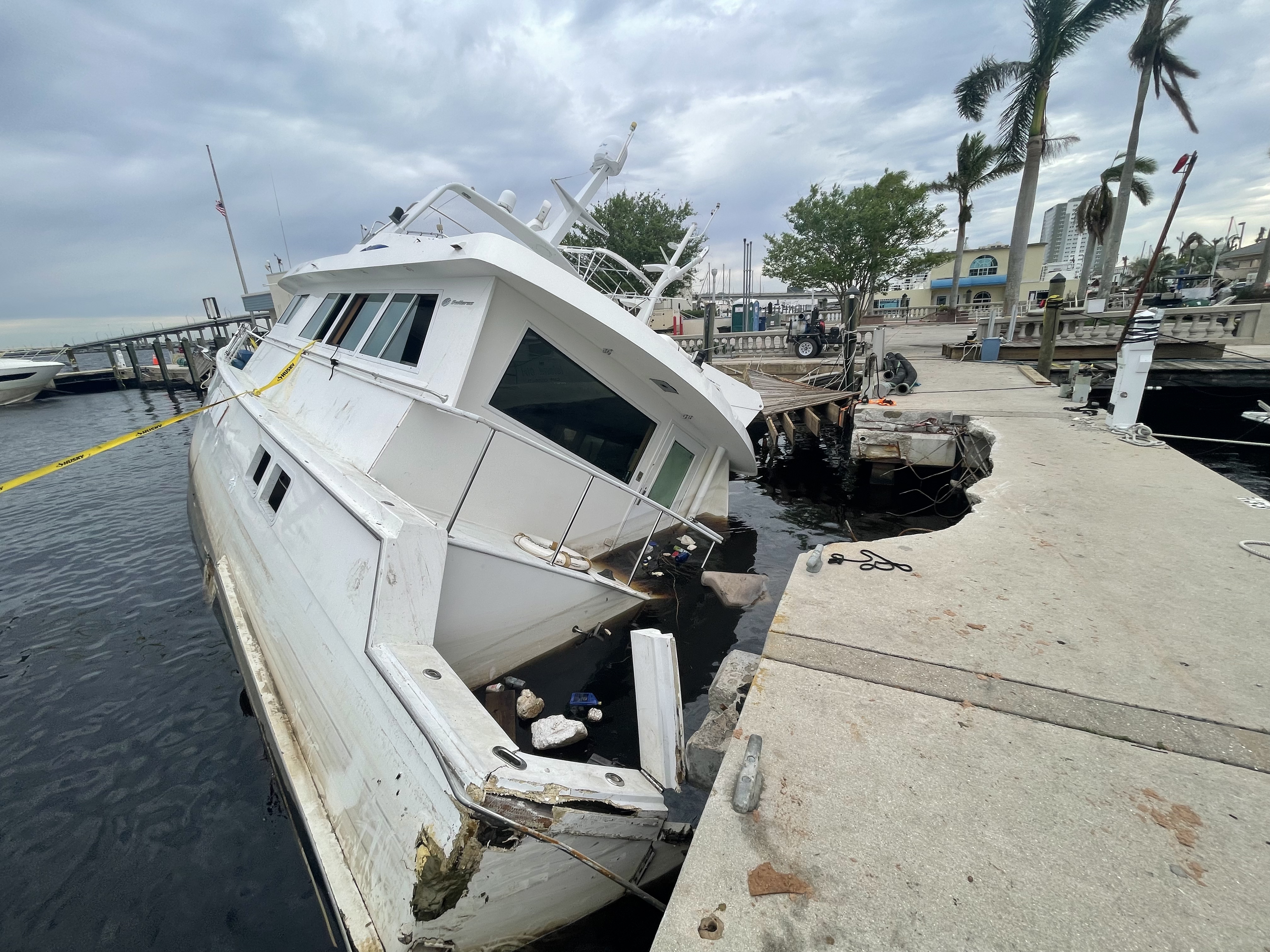 A half sunken abandoned derelict vessel that crashed into a marina walkway marked off with caution tape.