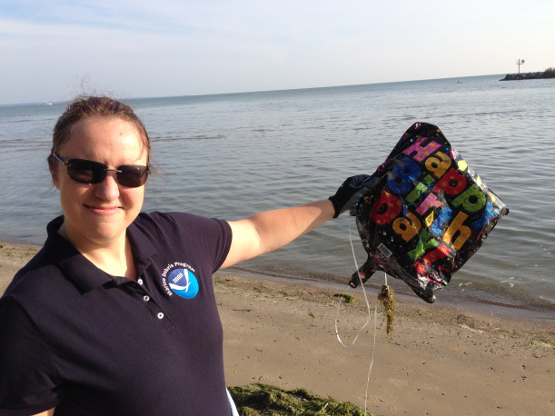 A person holding balloon debris that says "Happy Birthday!".