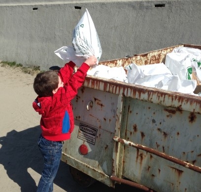 A child putting a bag of trash in a dumpster.