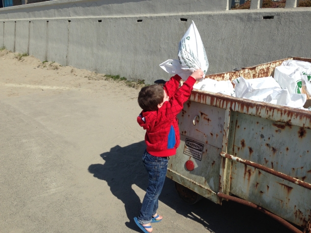 A young child putting a bag of trash into a dumpster.