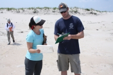 Two people monitoring a beach and adding debris information to a clipboard.