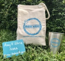 A reusable cotton lunch bag, wooden name tag, and metal cup.