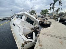 A half sunken vessel that crashed into a marina walkway surrounded by caution tape and debris.