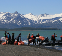 A cleanup crew moving debris into a boat with snowy mountain in the background.