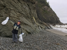 A beach cleanup volunteer holds bags of trash up in the air.