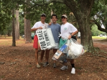 Three young men holding trash.