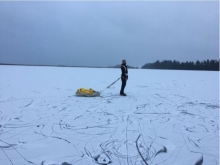 A person stands on a frozen lake pulling a yellow sled.