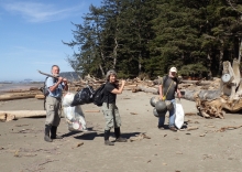 Three people carry several garbage bags filled with marine debris.