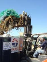  A person loads old fishing gear into a large metal bin by using a pallet jack.