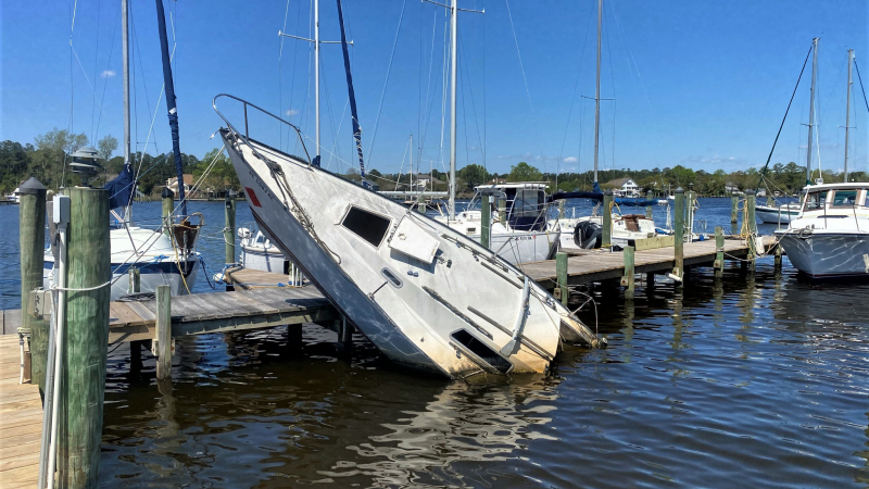 An abandoned sailboat stuck upright on the pilings of a dock.