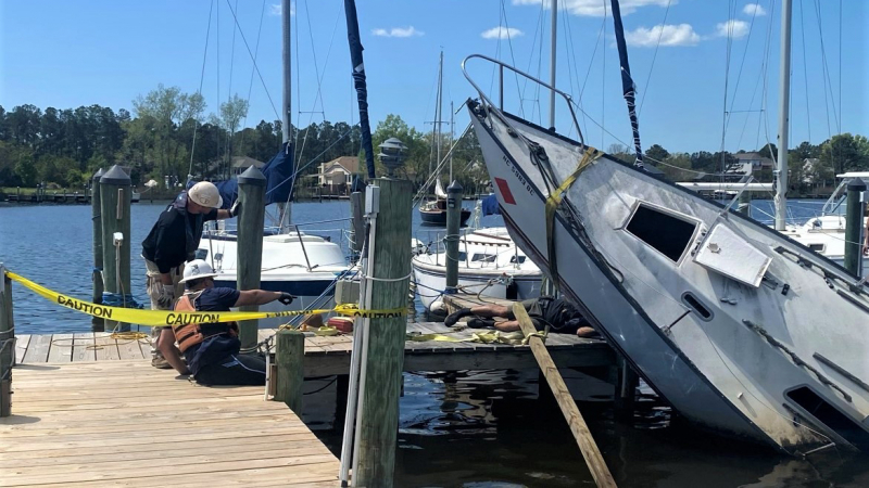 Contractors work on removing an abandoned sailboat stuck on the pilings of a dock.