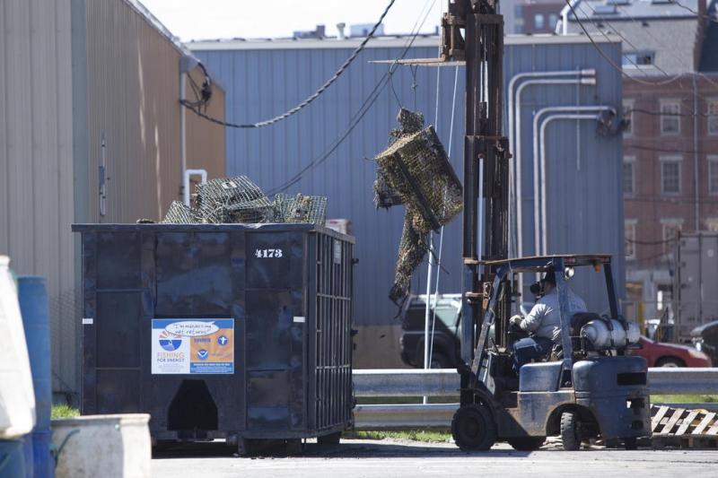 A person uses a forklift to place fishing nets into a dumpster.