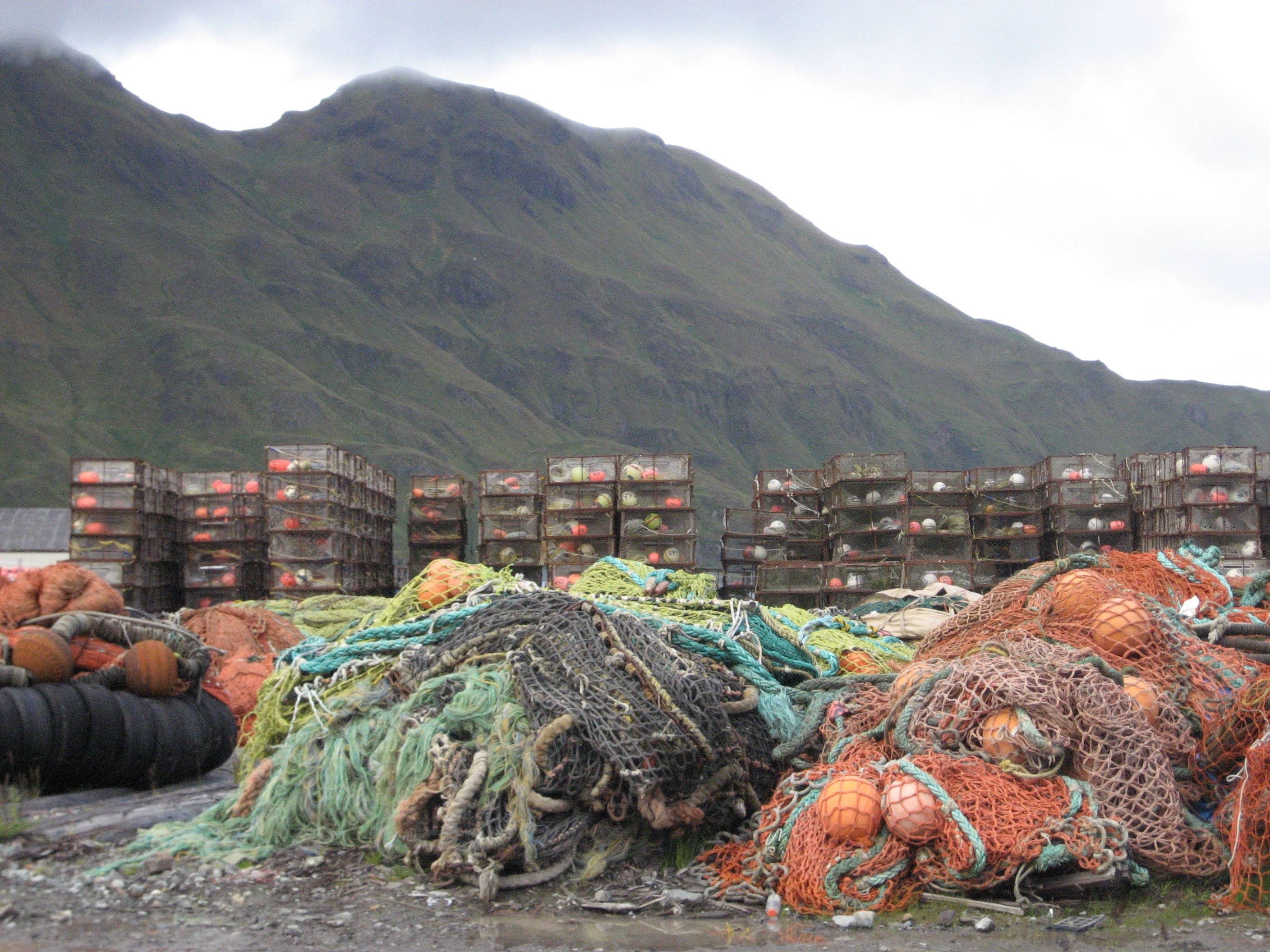 Stacks of crab traps and derelict fishing nets on the ground with a large mountain in the distance.