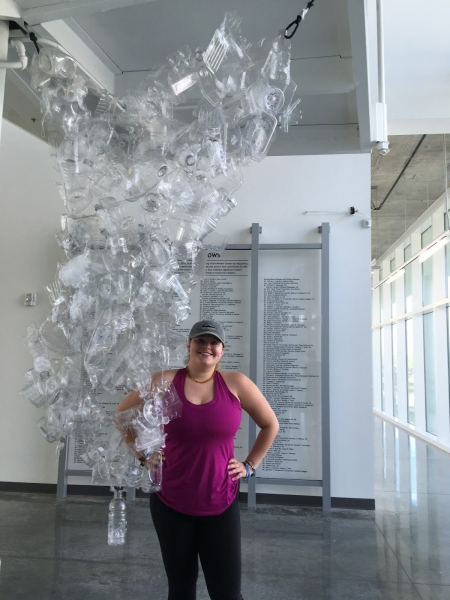 A woman stands near a collection of clear, plastic bottles that are hanging from the ceiling.