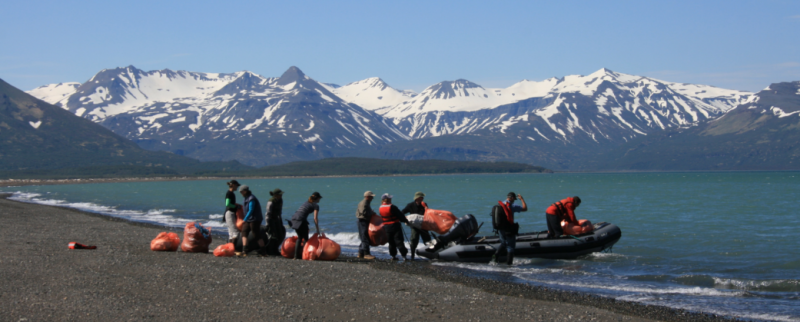 A cleanup crew moving debris into a boat with snowy mountain in the background.