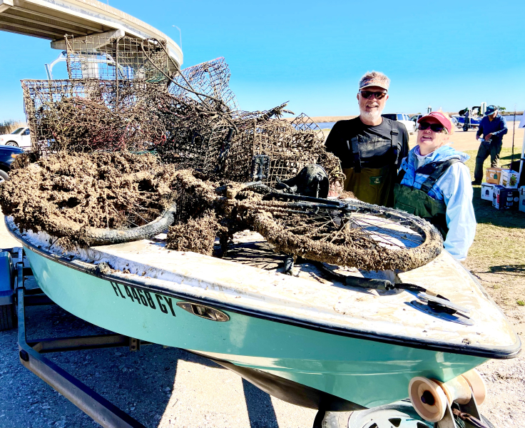 Two people standing next to their small boat filled with derelict fishing gear they recovered during an event.