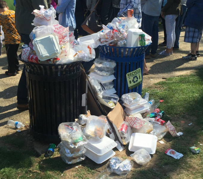 A pair of outdoor trash and recycling cans overflowing with trash.