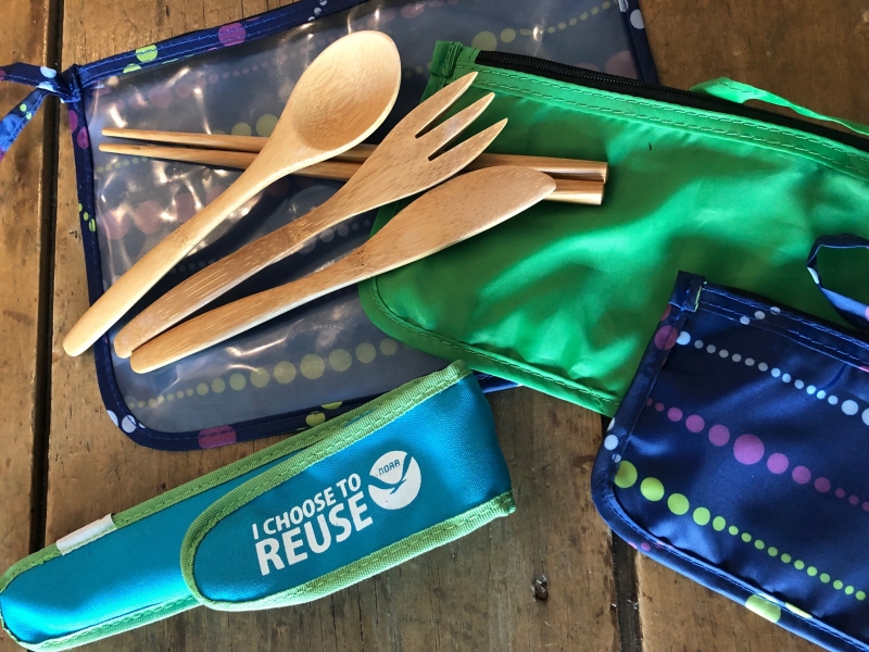 Reusable bamboo spoon, fork, and knife on top of reusable travel pouches. 