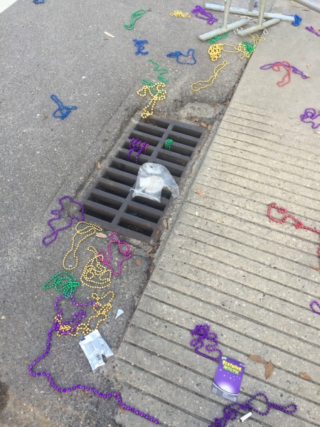 A gutter inside a street located in Louisiana is littered with aluminum cans and several beaded necklaces.