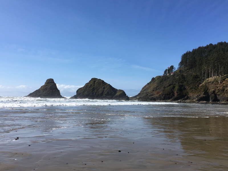 The shoreline of an Oregon beach with a lighthouse in the distance. 