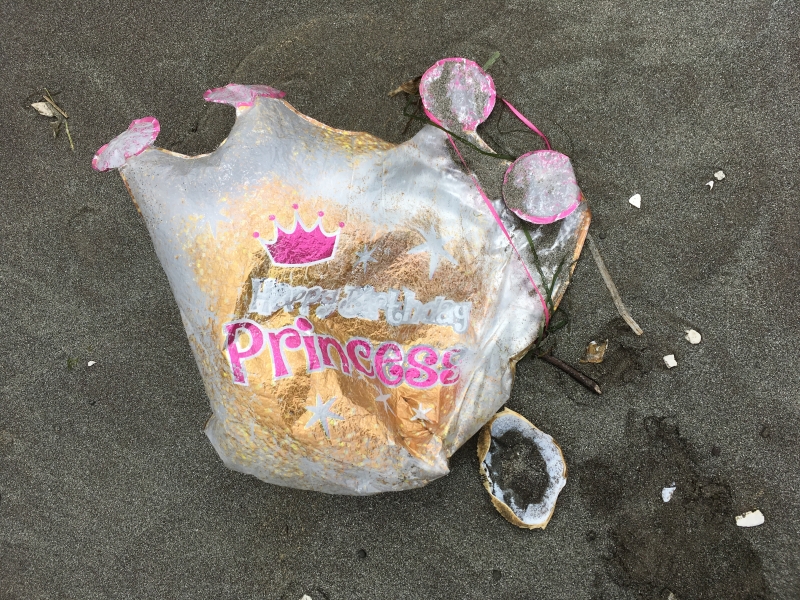A balloon in the shape of a crown lies on the beach with the title “princess” on it. 