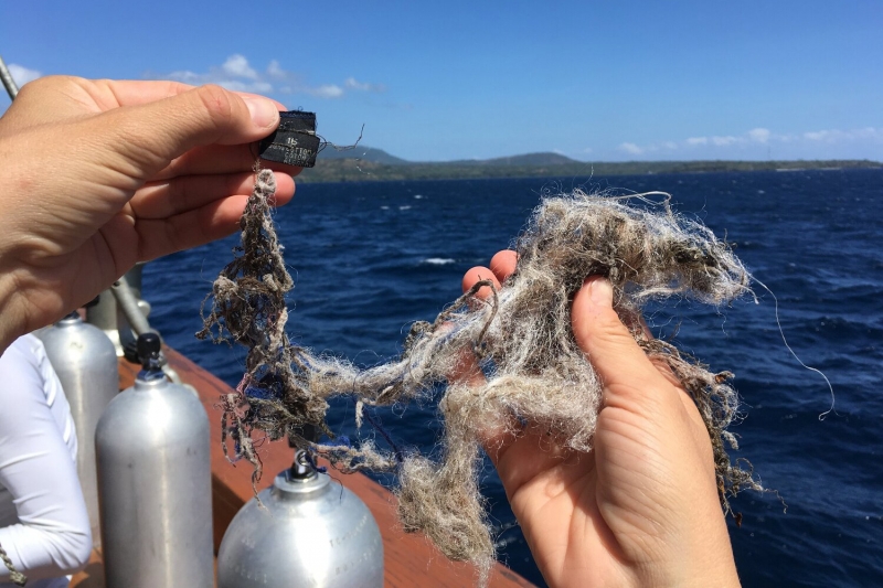 Hands holding a clothing label and a clump of microfibers pulled from the ocean.