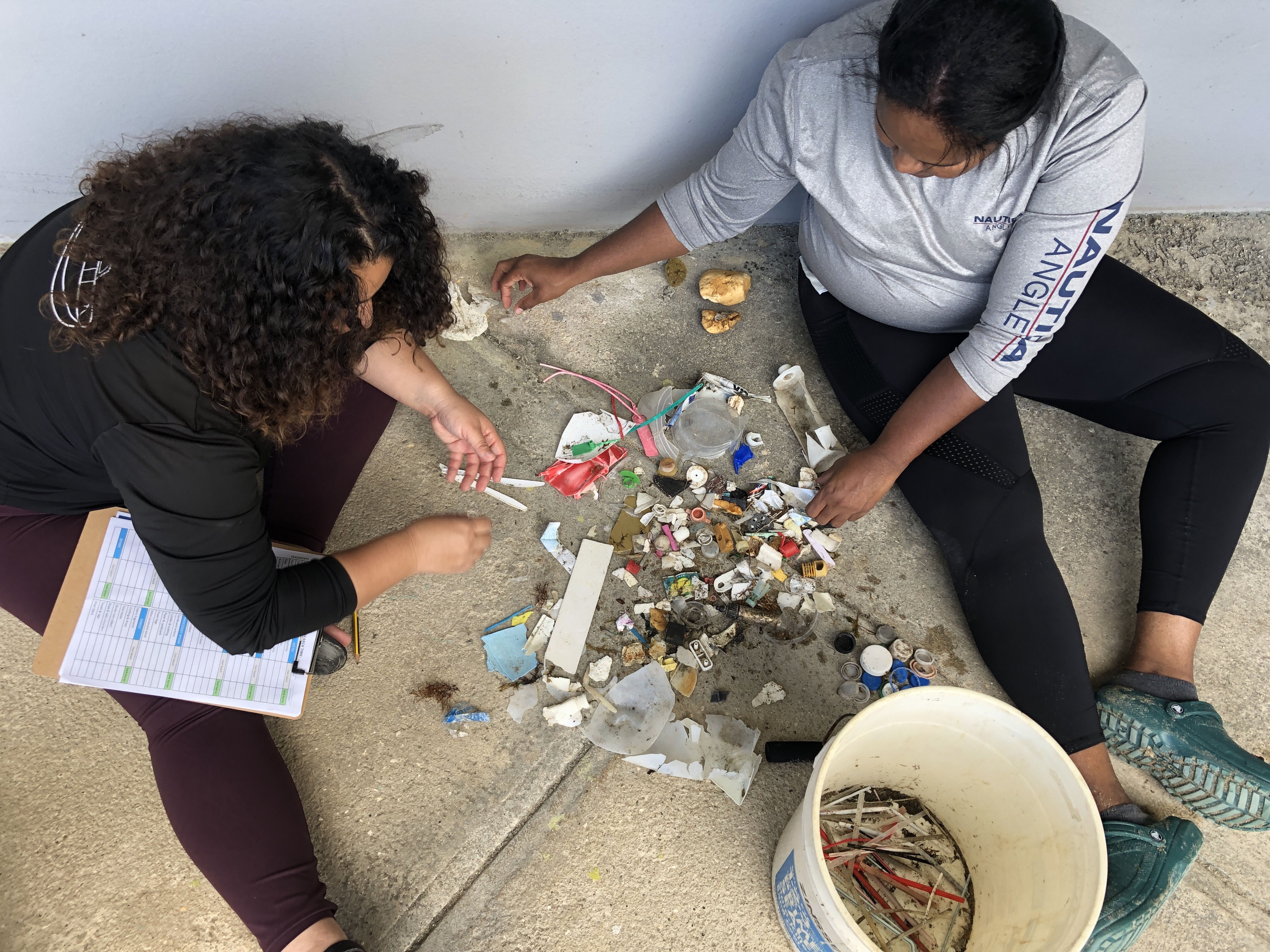 Two volunteers sorting through miscellaneous marine debris items and categorizing types of marine debris on a tracking sheet.