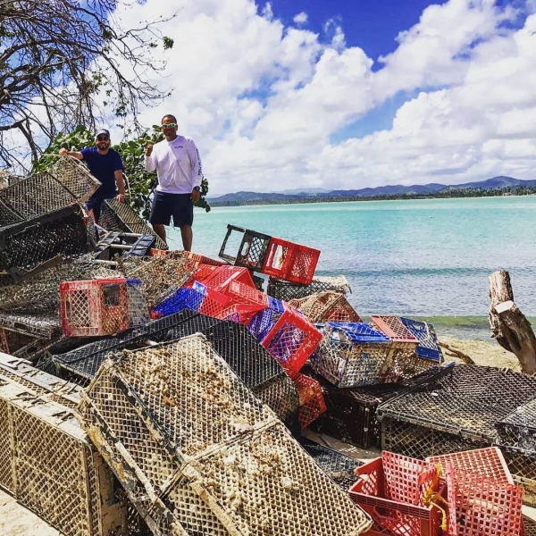 Two men stand on a beach next to a pile of collected crab traps.