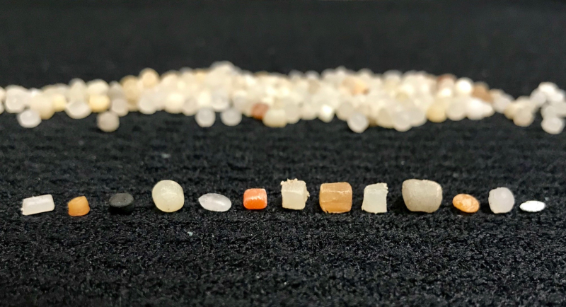 Small plastic pellets of different sizes, shapes, and colors lined up in a row.