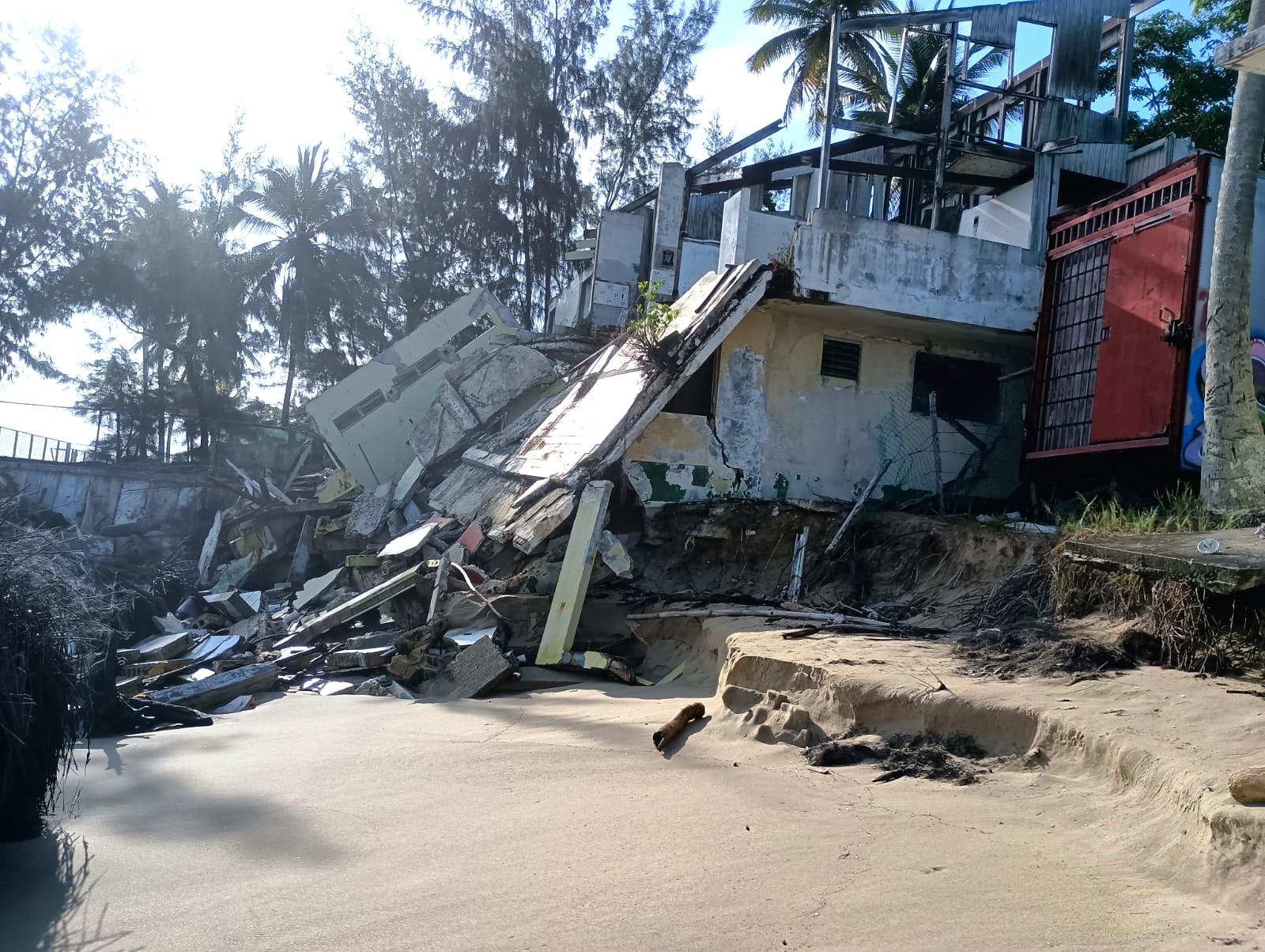 A dilapidated house structure on a tropical, sandy shoreline.