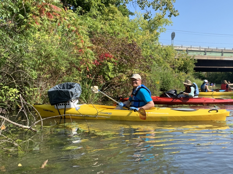 Three people, each in their own kayak, collect trash along a river.