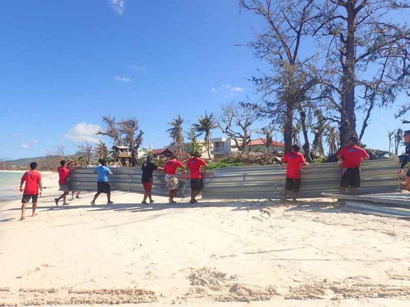 Community members work together to move tin panels off of a beach following a typhoon.