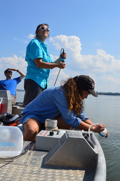 Two women and a man collect data on a boat.