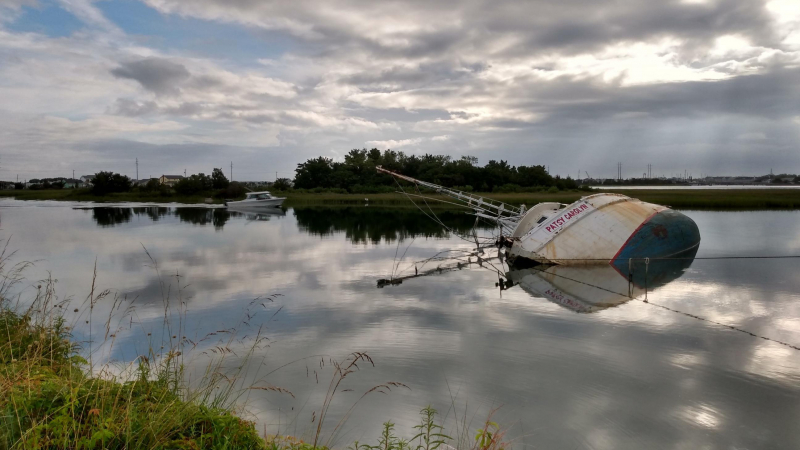 A partially submerged abandoned vessel on its side in the water.