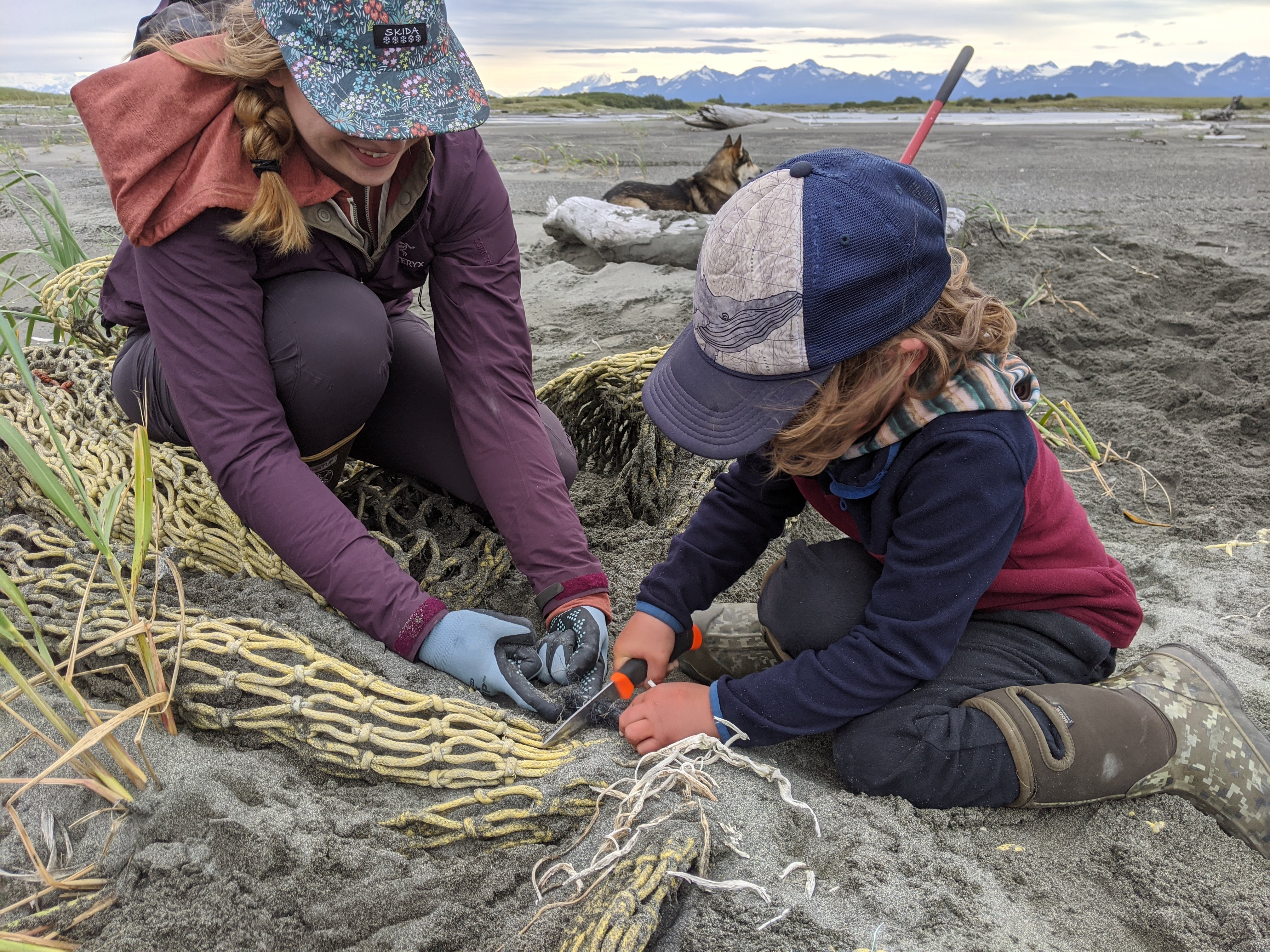 A woman and young girl cut netting apart that is partially unearthed from the sand.