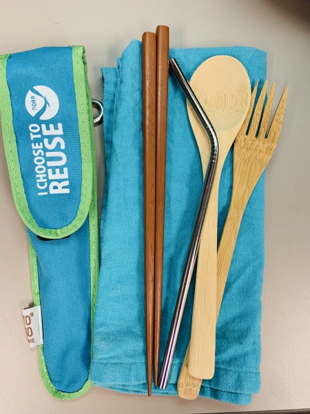 Bamboo silverware, chopsticks, and stainless steel straw rest on top of a cloth napkin.