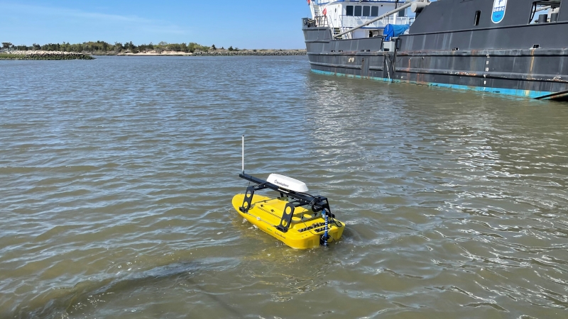 A small yellow autonomous vessel on the water mounted with a side-scan sonar device.