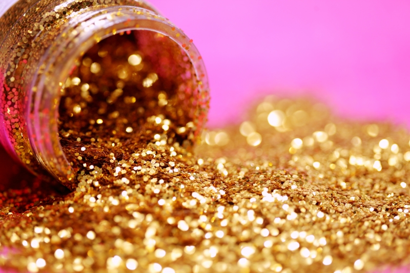 Gold glitter spills from a bottle onto a pink background.
