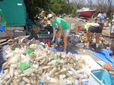 A woman standing next to lots and lots of collected plastic bottles.