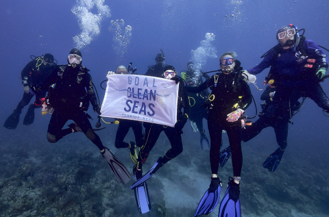 A team of divers underwater holding a sign that reads “Goal Clean Seas”.