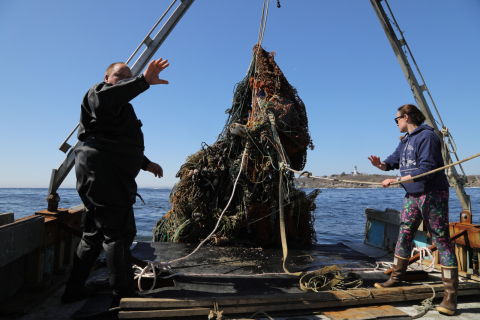 Two people on a boat hauling up a mass of old nets and other derelict fishing gear out of the water.