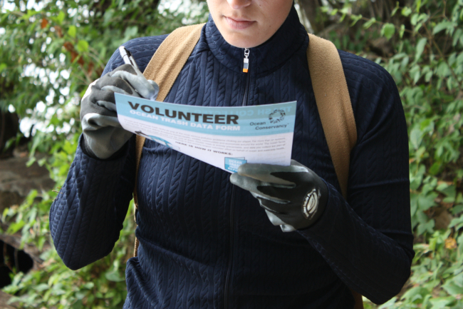 A person holding a volunteer datasheet and writing down the data from a trash cleanup.