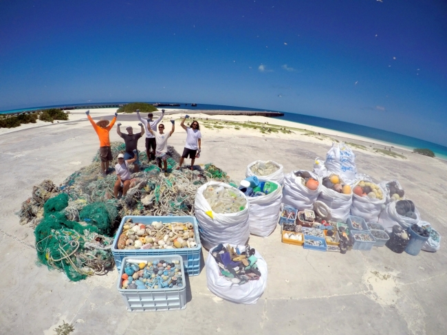 The marine debris mission team of seven stands tall among over 9 metric tons of derelict fishing gear and plastics removed from the shorelines of Midway Atoll.