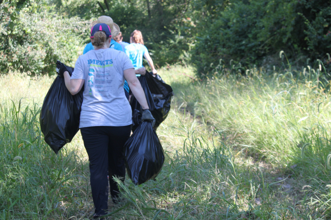 A group of people walking single file along a trail while carrying full, large black garbage bags. 