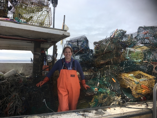 A person stands smiling on a boat that is full of derelict crab pots.