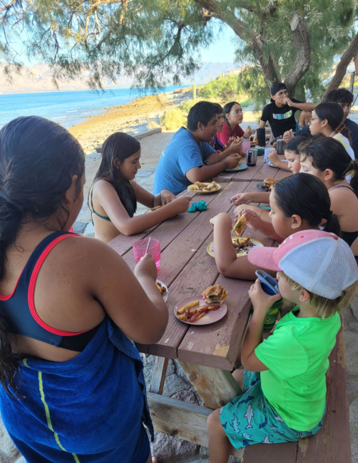 A group of people sit around a picnic table.