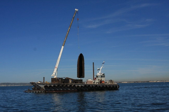 A derelict vessel being hauled out of the water with a crane.