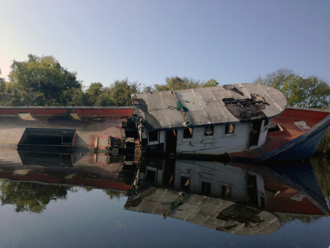 A damaged boat partially submerged on its side in the water.