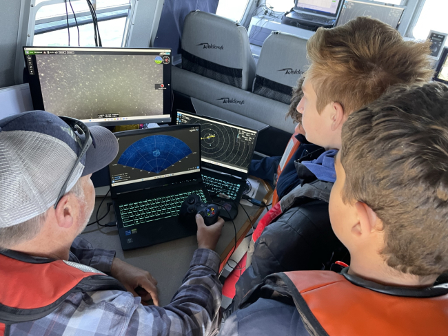 A group of students gathered around computers learning how to use sonar scanning devices.