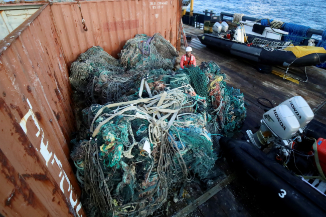 A marine debris removal team member stands next to large amounts of removed nets and debris.